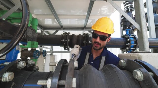 Two industrial technicians wearing safety helmets adjusting a large valve on heavy pipeline infrastructure at an industrial facility.