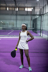 African American woman mid-30s white-dress posing on purple court balancing yellow ball on racket © wavebreak3