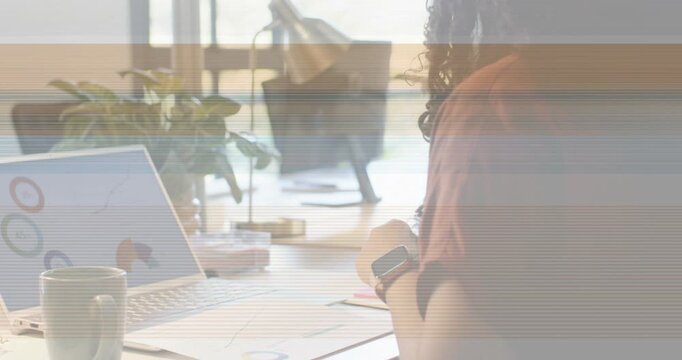 African American woman reviewing paper charts and laptop at desk in red top, scrolling smartphone