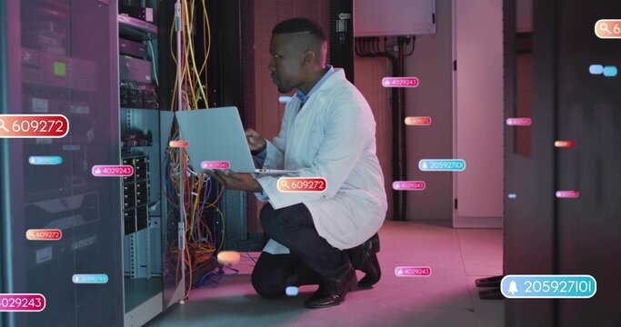 Kneeling tech in white lab coat inspecting rack in server room, laptop, cables, UI labels
