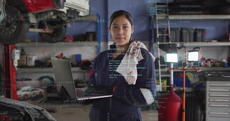 Naklejka premium Standing female mechanic holding laptop, checking codes in garage bay, rag on shoulder, lift lights