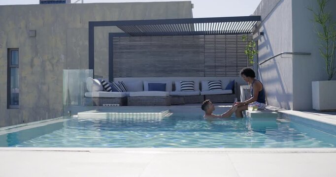Two men steadying partner in trunks placing legs in rooftop pool holding for balance, copy space
