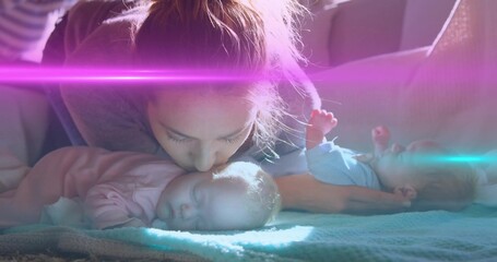 Kissing mother leaning over sleeping infant girls on couch, showing pink sleeper blue onesie © vectorfusionart