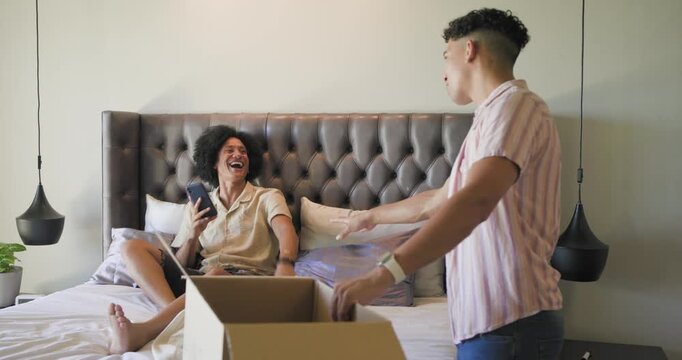 African American men pointing at moving box in bedroom, rummaging clothes and checking smartphone