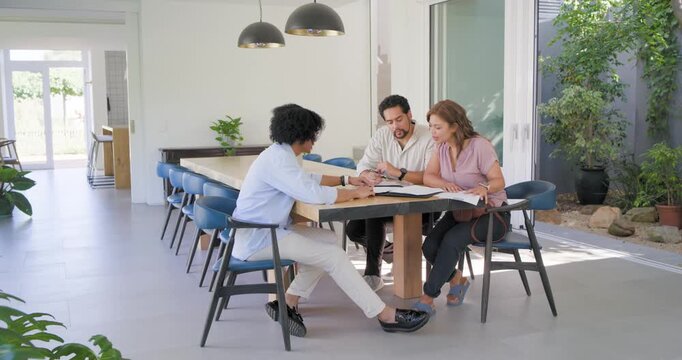 Couple leaning, advisor pointing at binder at dining table at home, man signing to finalize forms