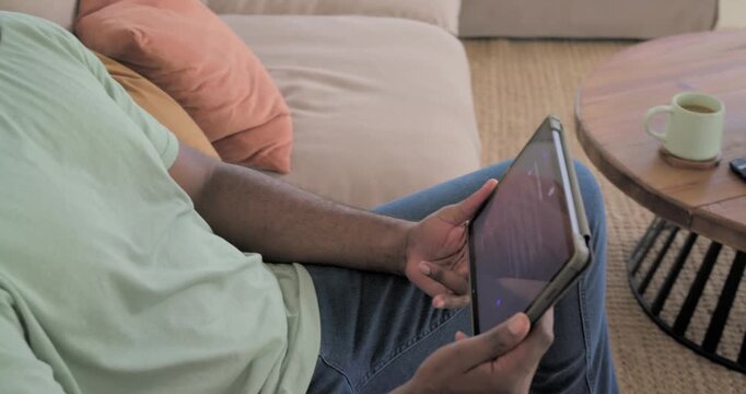 Man scrolling tablet on couch, causing camera pulling back, revealing smile while browsing tech