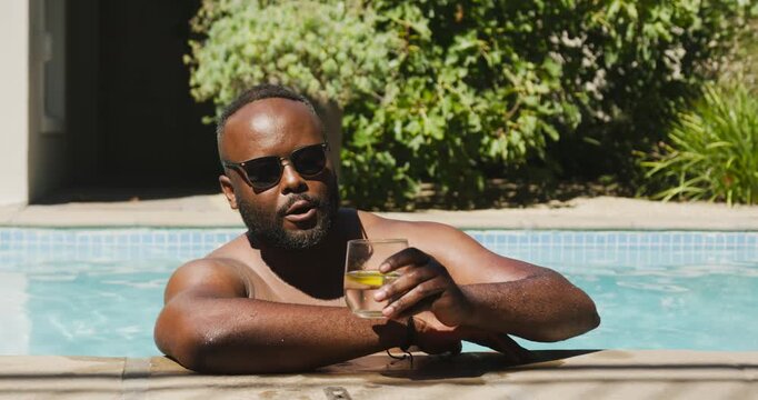 African man shirtless leaning poolside sipping lemon drink with shades noticing motion right