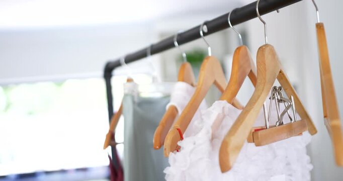 Camera pulling focus on black rail hangers revealing white ruffled garment near window showcasing
