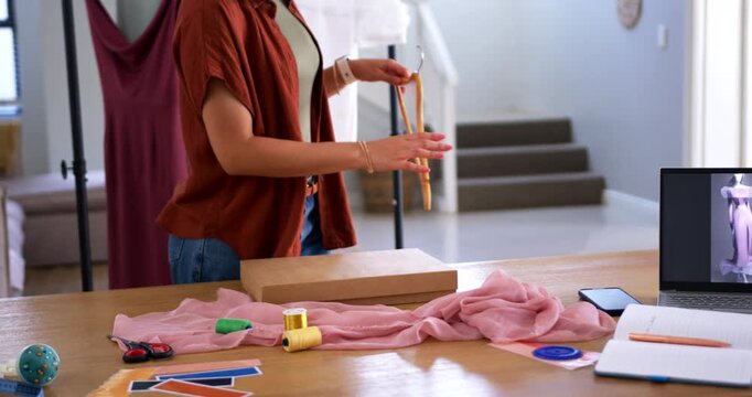 Adult woman placing box on drape at studio, reaching for hanger, picking ruffled top from rack