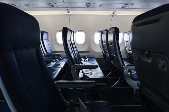 Empty airplane seats in cabin interior. Passenger transport concept and travel background. Modern aircraft seating. Commercial aviation interior with rows of seats and window light.