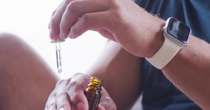 Adult man lifting dropper from amber bottle, releasing drops onto left hand at home testing skin