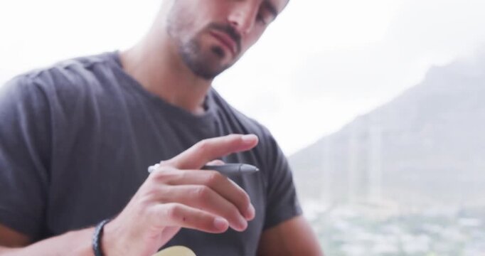 Man locating page in notebook, tapping pen and journaling beside window mountain view and wristband