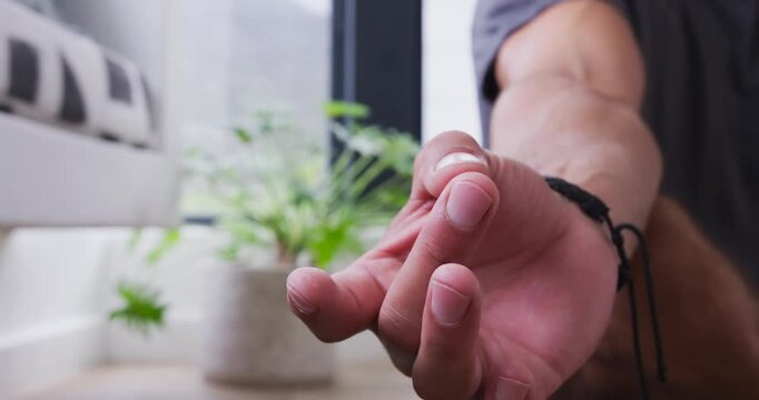 Lens focusing on hand, man rotating, pressing palms together by window, plant, couch in meditation