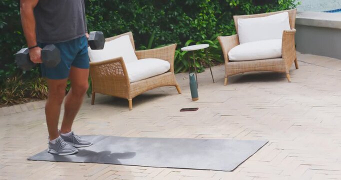 Adult man stepping onto mat, performing lunges with dumbbells, wearing grey t-shirt for strength