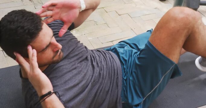 Man doing bike crunches starting supine on patio mat in sportswear for core with dumbbells bottle