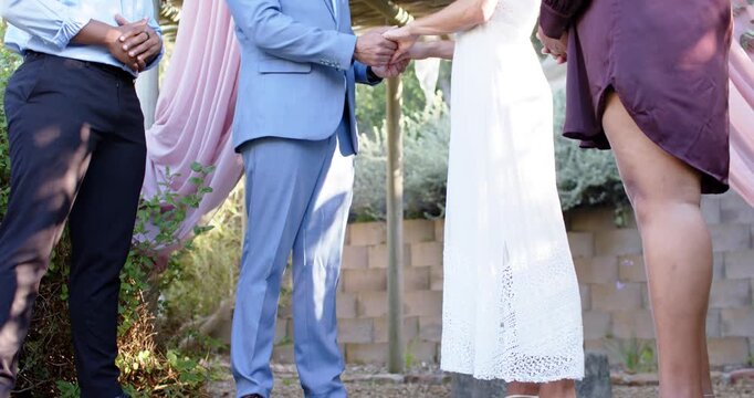 Couple stepping forward and clasping hands during vow exchange at garden pergola draped pale pink