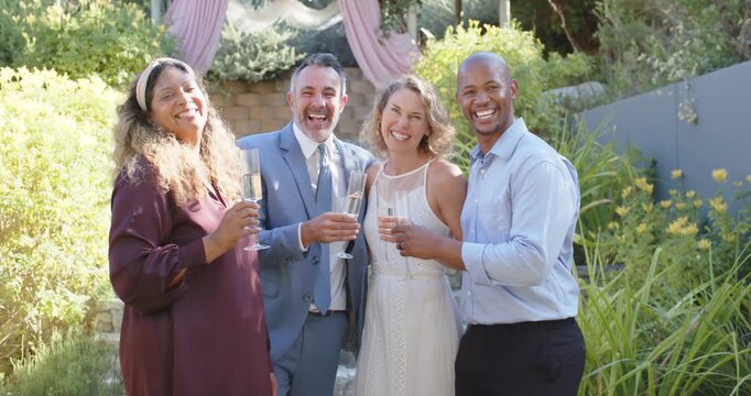 Wedding couple and two guests raising flutes for wedding toast, clinking, posing by pink arch