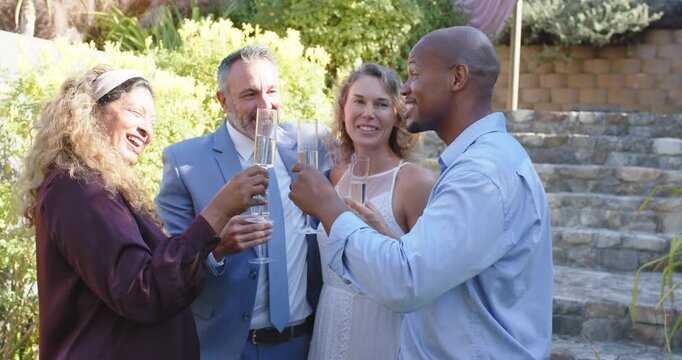 Diverse quartet celebrating in formal attire, raising champagne flutes, clinking, sipping in garden