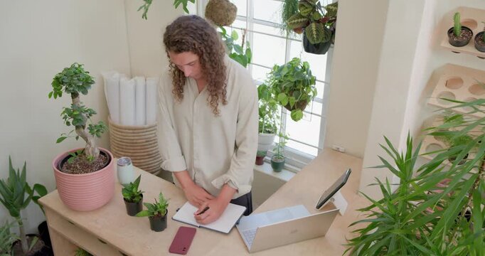 Nonbinary African American picking up pot inspecting and noting inventory in notebook at wood bench