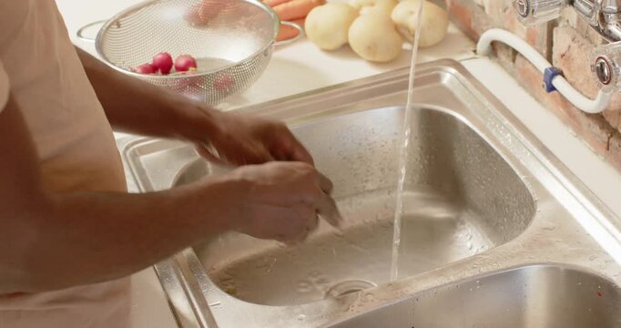 African man picking radishes from colander at kitchen sink, rinsing and rubbing for cooking