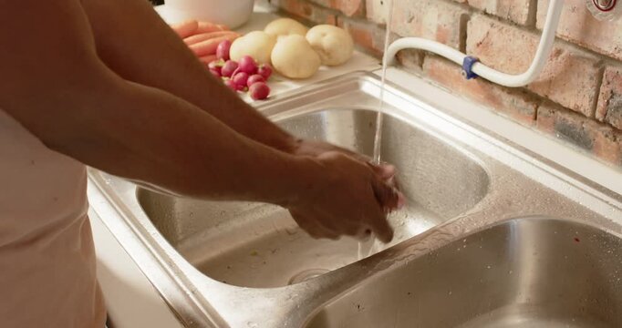 Adult man picking radish bunch and rinsing roots under running faucet for cooking at sink