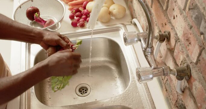 African man's hands turning on faucet, rinsing beetroot bunch at kitchen sink for cooking
