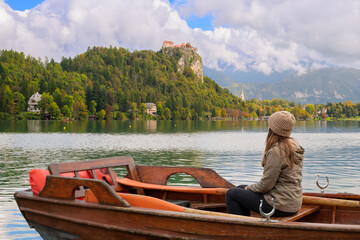 A young woman sits in a rented wooden rowboat on Lake Bled, with the medieval Bled Castle in the...