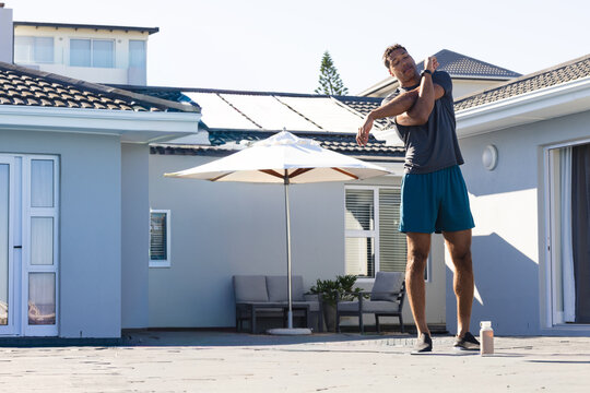 African American mid-adult man in sportswear stretching left arm on patio near shaker, copy space