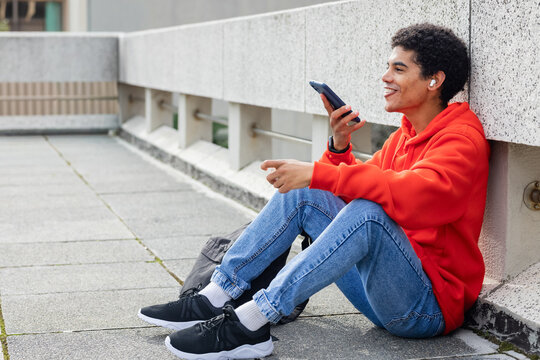 African American man sitting against rooftop parapet holding phone wearing earbuds, copy space