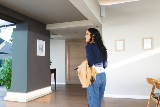 Woman standing by wooden front door looking back holding beige jacket and keychain, copy space