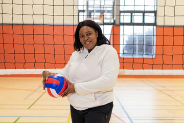 African American senior holding red-white-blue volleyball near net in gym wearing hoodie and pants © wavebreak3
