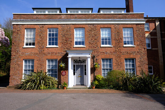 Exeter, United Kingdom  - March 22 2026. Bradninch Hall, a handsome Georgian red brick mansion in Exeter, adorned with hanging flower baskets and spring blossom.