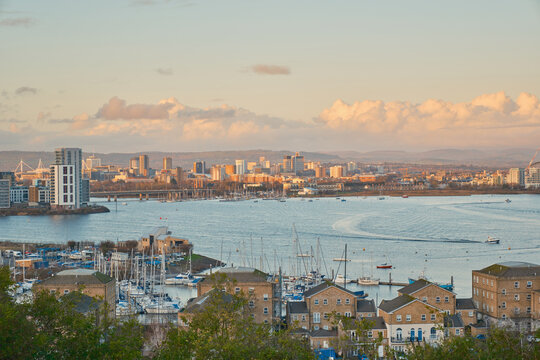 Cardiff  skyline at golden hour, with Penarth Marina's yachts and waterside apartments in the foreground under a cloud-scattered sky.