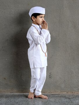 Indian boy in traditional Marathi attire with Gandhi cap and tulsi mala doing namaste, side profile, representing Warkari culture and Palkhi festival in a simple devotional pose.