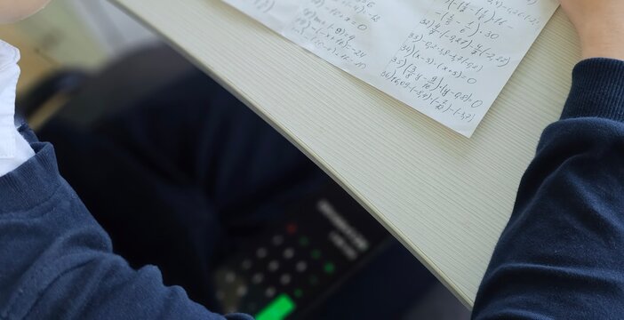 Student holding smartphone screen while taking math exam in school, concept of cheating in exam concept