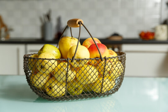 Fresh apples in metal wire fruit basket on kitchen table