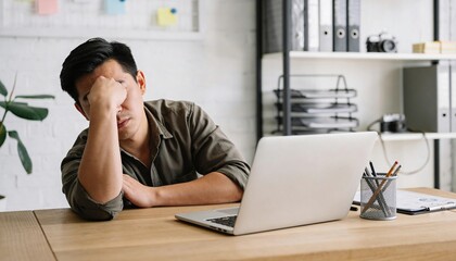 Exhausted man sitting at a table with a laptop rubbing tired eyes with one hand while resting his elbow, soft diffused light and neutral tones, realistic work burnout and stress lifestyle photography
