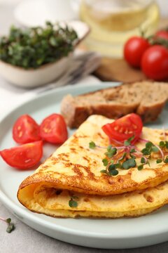 Tasty breakfast with omelette, microgreens, tomatoes, bread and oil on table, closeup