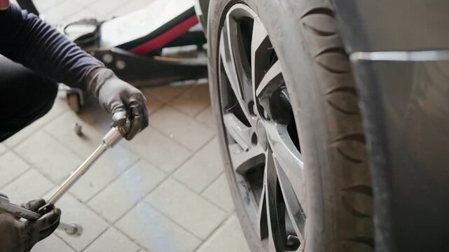 Professional car mechanic unscrewing lug nuts from a modern alloy wheel using a cross wrench during seasonal tire replacement service in a professional workshop, ensuring vehicle safety