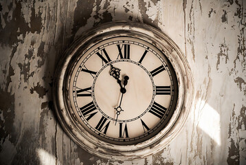 Fototapeta premium A vintage clock hangs on a weathered wooden wall, displaying 12:00.