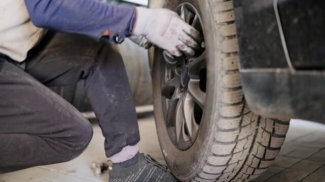 Close-up of an auto mechanic with safety gloves using a lug wrench to remove a wheel from a car during a seasonal tire change, revealing the brake disc assembly in a professional workshop