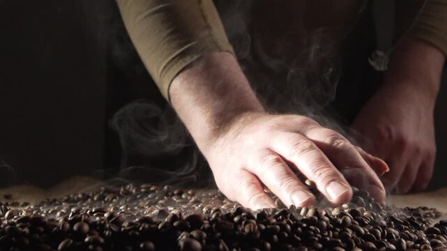 Concept of Coffee production industry. barista hands holds hot roasted fresh brown beans on table