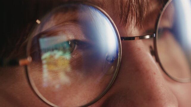 Close-up of a young woman wearing glasses, scrolling social media on her smartphone, with the screen reflected in her lenses.
