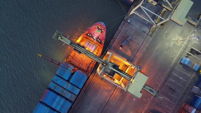 Container crane loading cargo ship at a busy port terminal at night with illuminated industrial activity