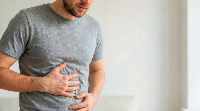 Man holding his stomach in pain. Adult male rubbing belly experiencing indigestion or nausea. Healthcare and medical concept. Copy space for text