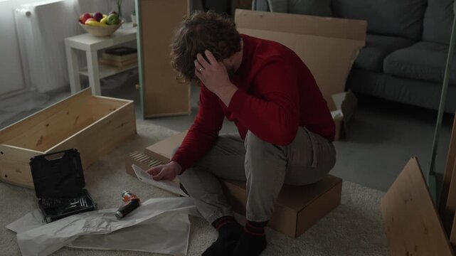 Frustrated man assembling furniture following complicated instructions