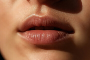 Fototapeta premium Subject: A close-up of a person’s lips. Action: The lips are slightly parted, appearing natural and hydrated. Setting: An indoor setting with focused lighting on the face.