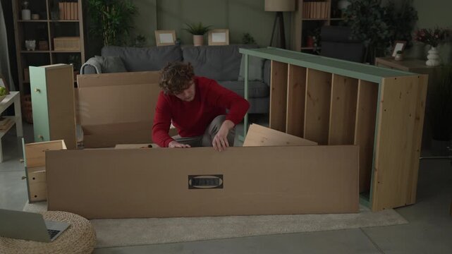 Young man assembling new wooden furniture in living room