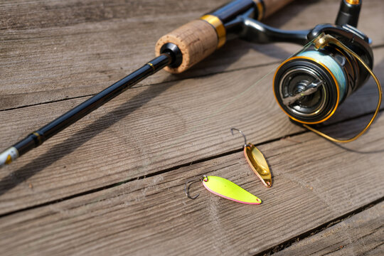 A spinning rod with a reel and fishing lures lies on an old wooden table.