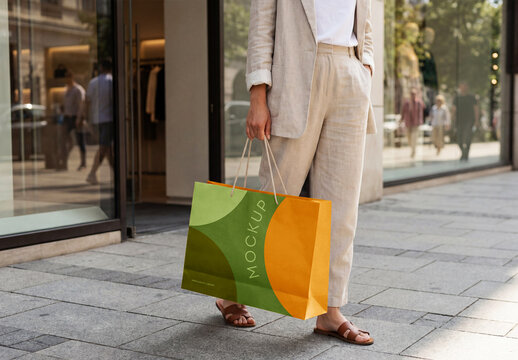 Perspective View Of A Woman Carrying A Large White Paper Bag Mockup On A City Sidewalk, Blank Shopping Bag Template For Branding